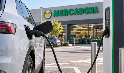 Coche eléctrico blanco cargando en un puesto de carga frente a un supermercado Mercadona.