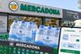 Teléfono móvil mostrando la aplicación de compra online de Mercadona frente a un supermercado y varios packs de agua mineral.