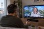 Hombre sentado frente a un televisor con interferencias y píxeles en la imagen.