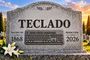 Lápida de piedra en un cementerio con la palabra TECLADO grabada y un dibujo de un teclado de ordenador.