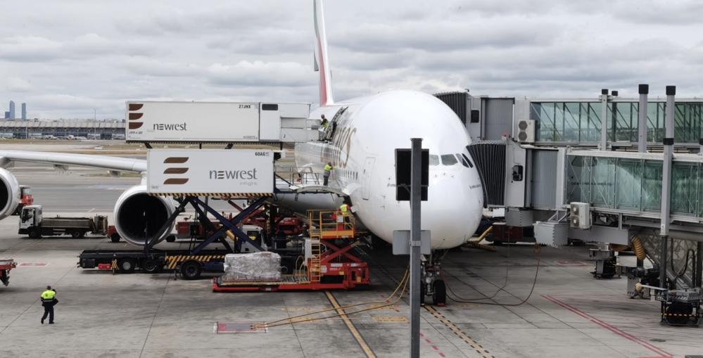 Avión de pasajeros estacionado en la terminal recibiendo suministros de catering de Newrest mediante camiones elevadores.