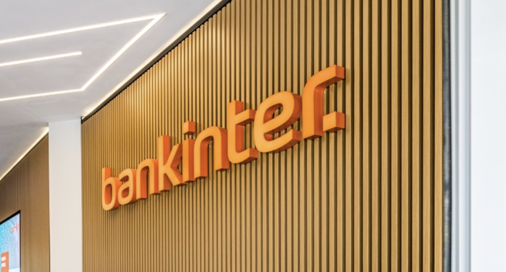 Logotipo de Bankinter en letras naranjas con relieve sobre una pared de listones de madera verticales.