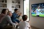 Grupo de personas de distintas edades celebrando un gol frente a un televisor en un salón.