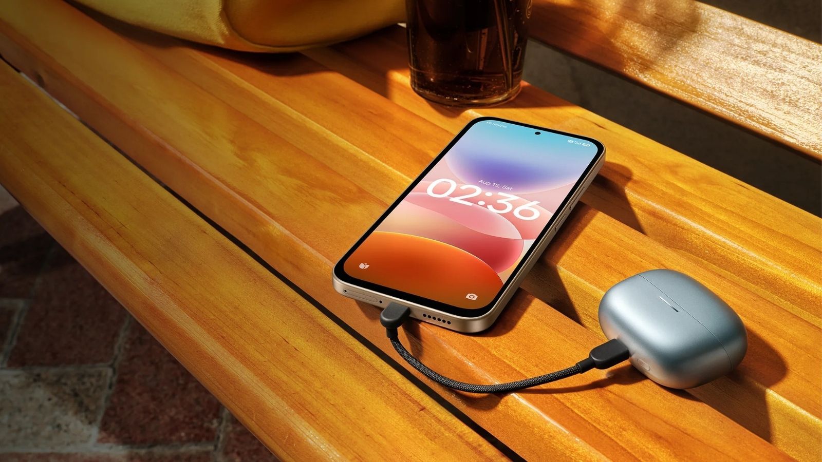 Teléfono inteligente conectado mediante cable USB-C a un estuche de auriculares inalámbricos sobre un banco de madera.