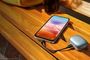 Teléfono inteligente conectado mediante cable USB-C a un estuche de auriculares inalámbricos sobre un banco de madera.