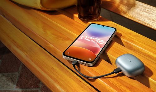 Teléfono inteligente conectado mediante cable USB-C a un estuche de auriculares inalámbricos sobre un banco de madera.