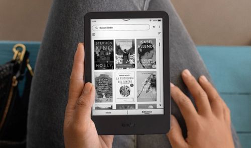 Primer plano de una persona sosteniendo un lector electrónico Kindle con la biblioteca de libros digitales en pantalla.