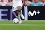 Primer plano de las piernas de un futbolista con el balón y el logotipo de Movistar Plus+ al fondo.