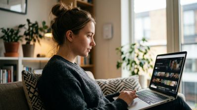 Mujer joven sentada en un sofá utilizando un ordenador portátil para ver contenidos en streaming.