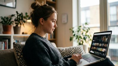 Mujer joven sentada en un sofá utilizando un ordenador portátil para ver contenidos en streaming.