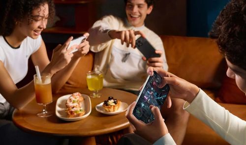 Tres personas usando teléfonos móviles mientras meriendan en un sofá.