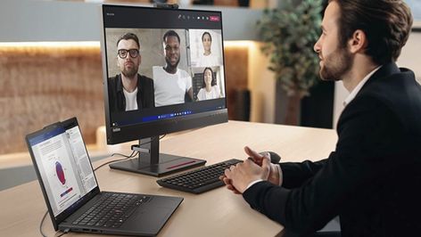Usuario en una oficina realizando una videollamada grupal con un portátil Lenovo conectado a un monitor externo.