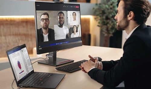 Usuario en una oficina realizando una videollamada grupal con un portátil Lenovo conectado a un monitor externo.