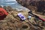 Teléfono Redmi Note 17 cargando unos auriculares inalámbricos sobre una roca en la costa.