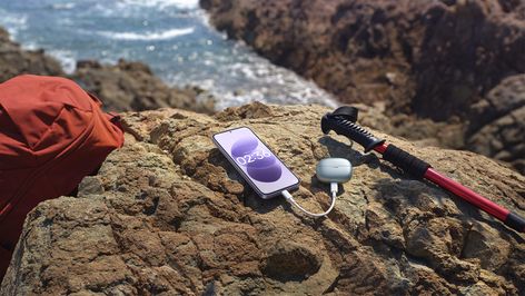 Teléfono Redmi Note 17 cargando unos auriculares inalámbricos sobre una roca en la costa.