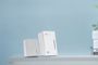 Dos dispositivos PLC de TP-Link de color blanco sobre un mueble frente a una pared azul.