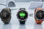Tres relojes inteligentes Garmin Fenix 9 en color beige, negro y naranja sobre una mesa, el central muestra un aviso de actualización de software instalada y mejora de batería.