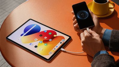 Tableta Redmi Pad 2 Pro cargando un teléfono móvil mediante conexión por cable sobre una mesa naranja.