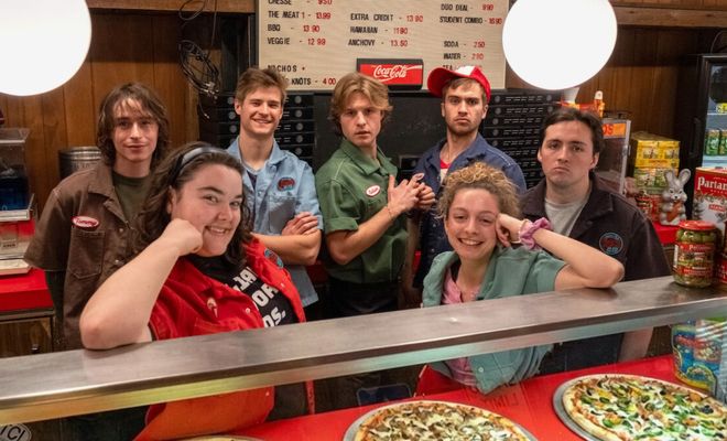 Grupo de jóvenes trabajadores posando tras el mostrador de una pizzería.
