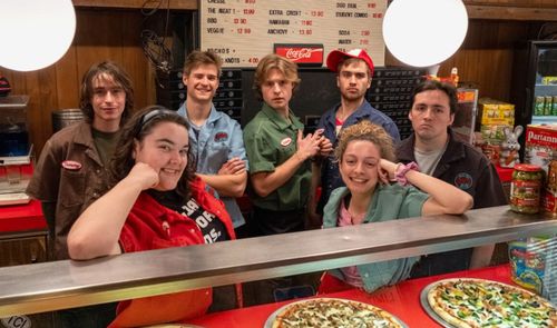 Grupo de jóvenes trabajadores posando tras el mostrador de una pizzería.