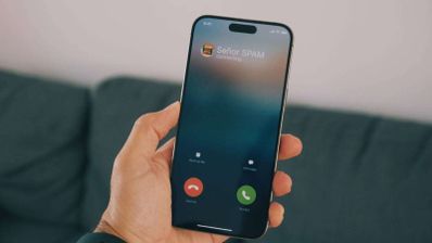Mano sujetando un teléfono móvil que muestra una llamada entrante identificada como correo no deseado o spam.