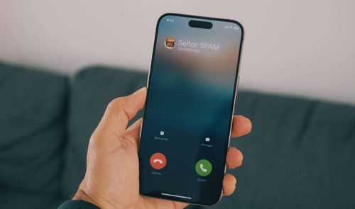 Mano sujetando un teléfono móvil que muestra una llamada entrante identificada como correo no deseado o spam.