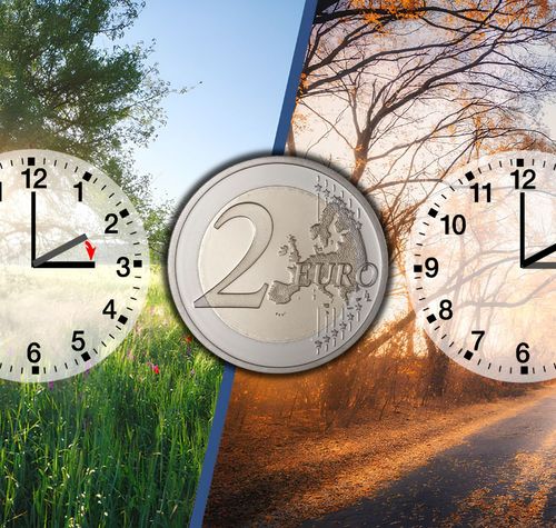 Composición de dos relojes marcando el cambio de hora entre verano e invierno junto a una moneda de dos euros.