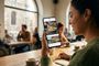 Una mujer joven en una cafetería consultando la aplicación de Facebook en su teléfono móvil.