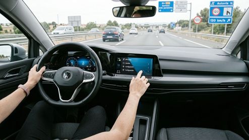 Conductor interactuando con la pantalla central de un coche que circula por autopista.