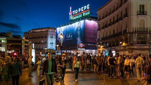 Personas caminando por la Puerta del Sol de Madrid al anochecer con el icónico cartel luminoso de Tío Pepe de fondo.