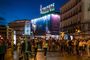 Personas caminando por la Puerta del Sol de Madrid al anochecer con el icónico cartel luminoso de Tío Pepe de fondo.