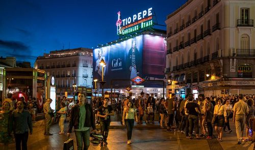 Personas caminando por la Puerta del Sol de Madrid al anochecer con el icónico cartel luminoso de Tío Pepe de fondo.