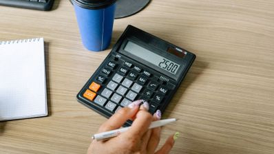 Persona utilizando una calculadora de escritorio junto a un cuaderno y un bolígrafo en una oficina.