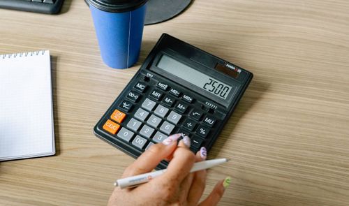 Persona utilizando una calculadora de escritorio junto a un cuaderno y un bolígrafo en una oficina.