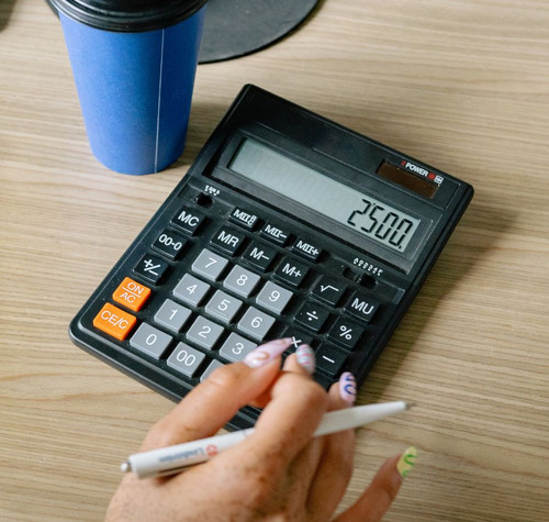 Persona utilizando una calculadora de escritorio junto a un cuaderno y un bolígrafo en una oficina.