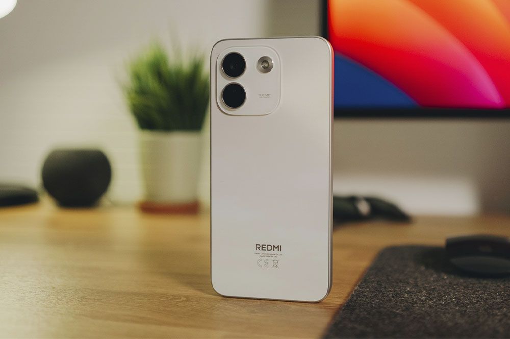 Parte trasera de un teléfono móvil Redmi en color blanco sobre un escritorio de madera.