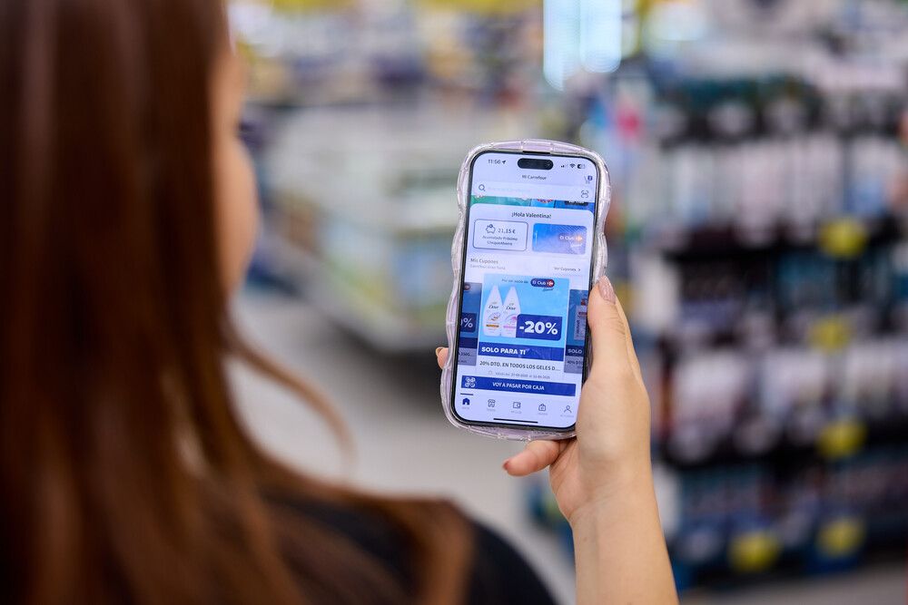 Persona consultando promociones y descuentos en la aplicación de Carrefour desde su teléfono móvil dentro de un supermercado.