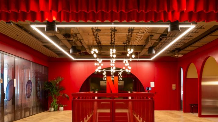 Interior de unas oficinas de Netflix con paredes rojas, techos industriales y una gran N roja al fondo.