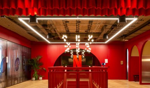 Interior de unas oficinas de Netflix con paredes rojas, techos industriales y una gran N roja al fondo.