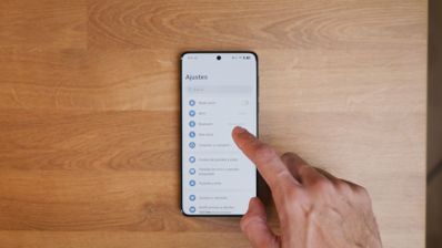 Dedo pulsando el menú de Ajustes en la pantalla de un teléfono Android sobre una mesa de madera.