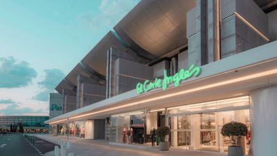 Fachada exterior de un centro comercial El Corte Inglés con el logotipo iluminado en verde sobre la entrada principal.