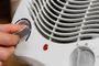 Primer plano de una mano ajustando el selector de potencia en un calefactor eléctrico portátil de color blanco.