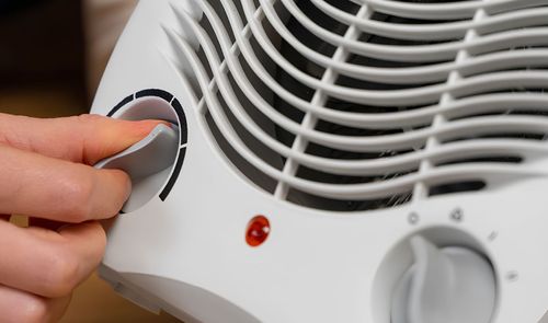 Primer plano de una mano ajustando el selector de potencia en un calefactor eléctrico portátil de color blanco.