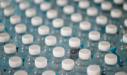 Primer plano de hileras de botellas de plástico transparente con tapones blancos en una planta de producción.