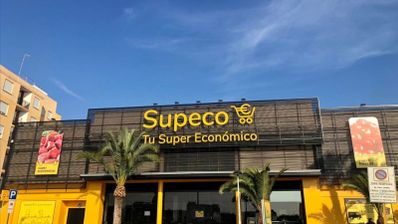 Fachada exterior de un supermercado Supeco con su logotipo amarillo sobre fondo oscuro.