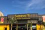 Fachada exterior de un supermercado Supeco con su logotipo amarillo sobre fondo oscuro.