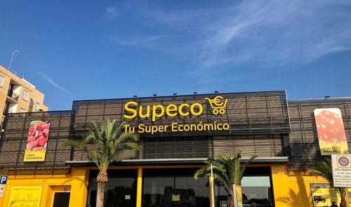 Fachada exterior de un supermercado Supeco con su logotipo amarillo sobre fondo oscuro.