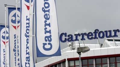 Banderas blancas con el logotipo azul y rojo de Carrefour frente a la fachada de un establecimiento