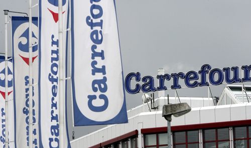 Banderas blancas con el logotipo azul y rojo de Carrefour frente a la fachada de un establecimiento