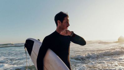 Surfista consultando su reloj inteligente en la orilla del mar al atardecer.